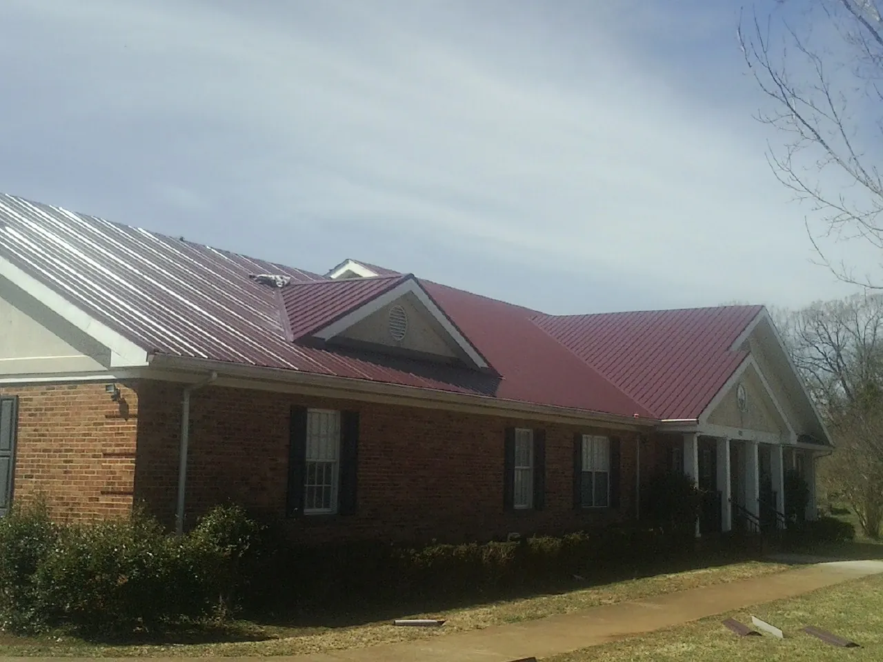 Red metal roof with gabled entries on a long brick building, from a Hail Damage Roof Repair job in Americus