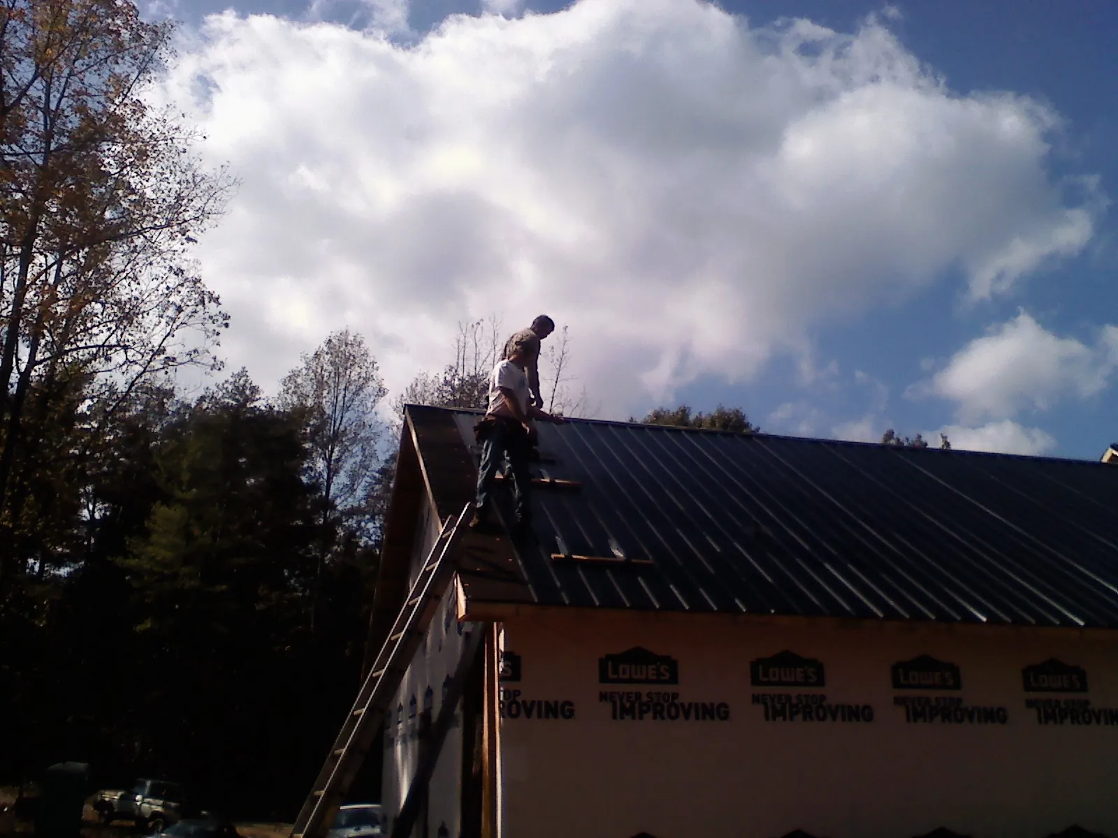 Roofer fastening dark metal panels high against a cloudy sky, from a Roof Inspection job in Americus