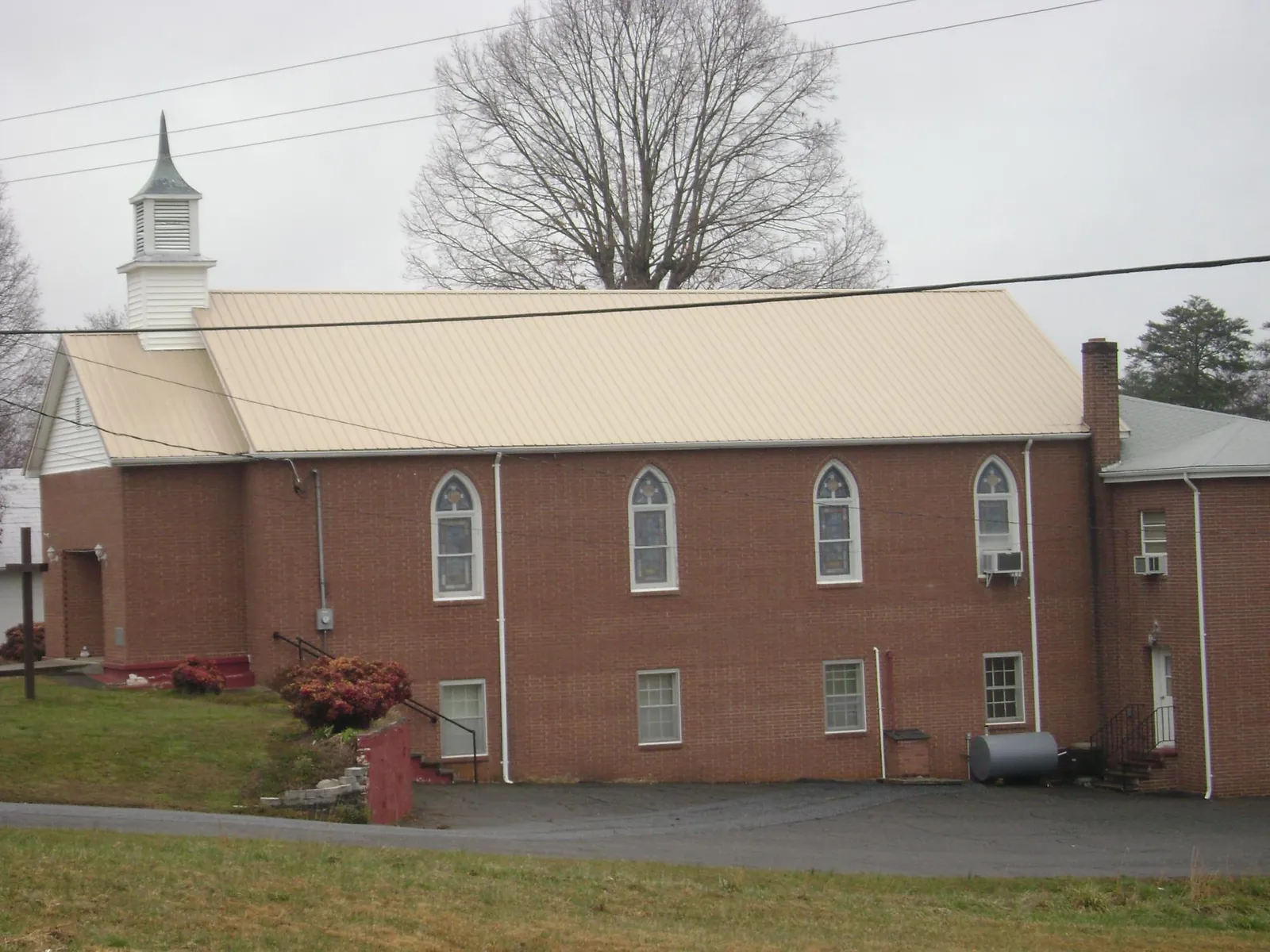 New tan metal roof on a brick church with a white steeple in Americus