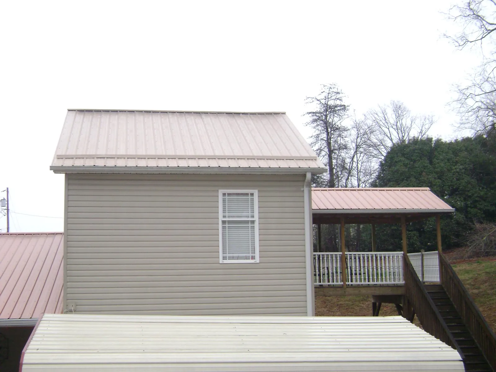 Tan metal roofs on a two story addition and attached porch, from a Roof Replacement job in Americus